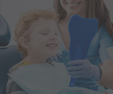 Child in dental chair looking at smile in mirror