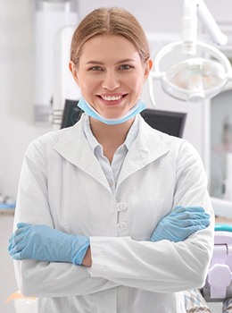 A female dentist wear personal protective equipment while folding her arms and smiling at the camera
