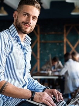 A young man working on a laptop and smiling after seeing his MetLife dentist in Virginia Beach