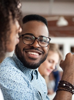 A young man wearing glasses listening to his colleague speak while working on a project