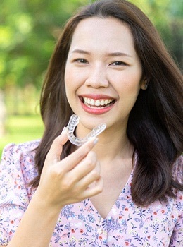 A woman smiling and holding an Invisalign aligner